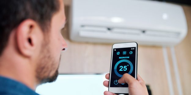 Young man using smart application to adjust temperature of air conditioning after servicing